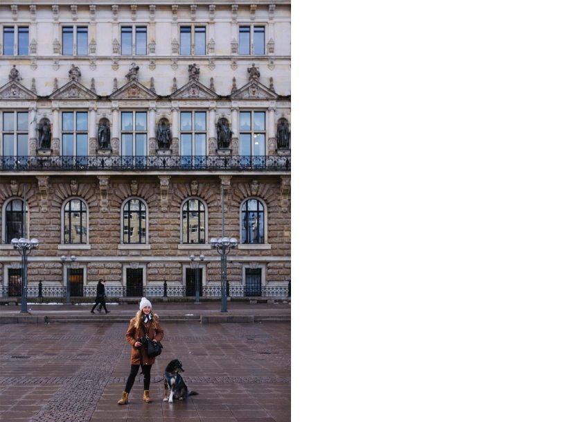 Eine Person und ein Hund stehen vor dem Hamburger Rathaus.